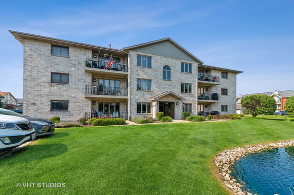 Front view of a multi-story brick apartment building with balconies and a landscaped lawn.