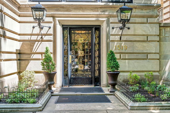 Front entrance of a building with a decorative glass door flanked by two lanterns and potted plants.