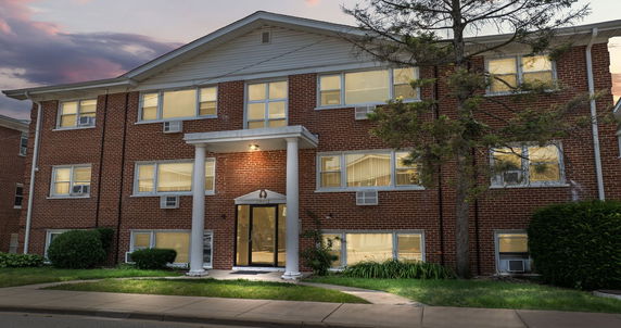 Front view of a multi-story brick building with illuminated windows and entrance.