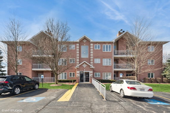 Front view of a multi-story brick apartment building with balconies and an entrance.