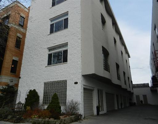 Front view of a multi-story building with a white exterior and garage units on the ground floor.