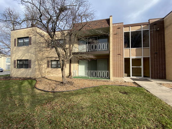 Front view of a two-story brick apartment building with balconies and a glass entry door.