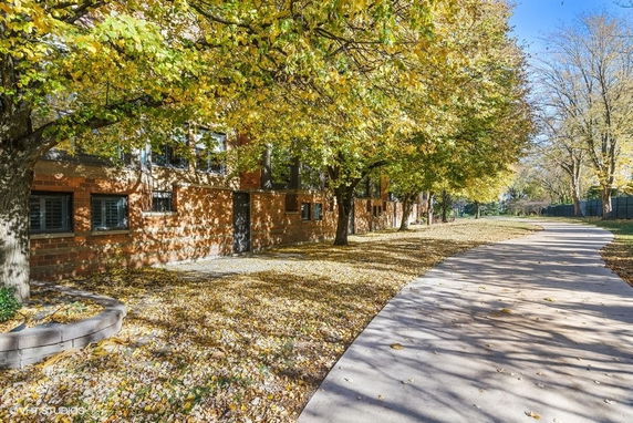 Front view of a brick building partially obscured by trees with a sidewalk in front.