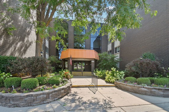 Front view of a multi-story building with a landscaped entrance and glass windows.