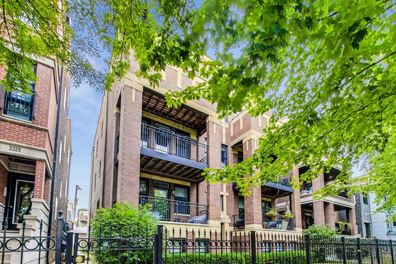 Front view of a multi-story brick building with balconies and a metal fence.