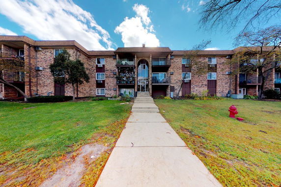 Front view of a multi-story brick apartment building with balconies.