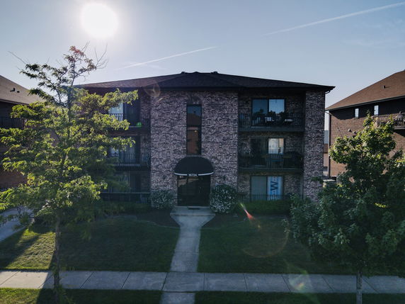 Front view of a three-story brick apartment building with balconies.