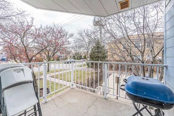Outdoor view from a balcony showing a residential street and trees.