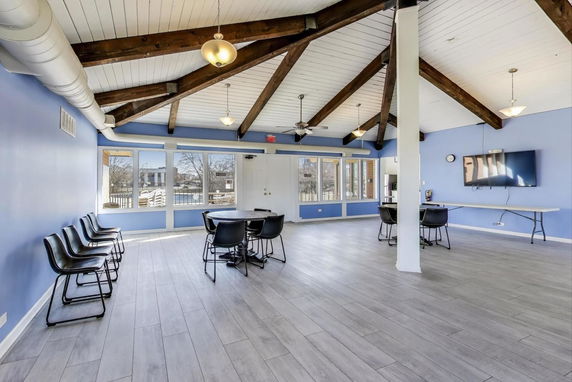Room with wooden beams, large windows, and tables for recreational activities.