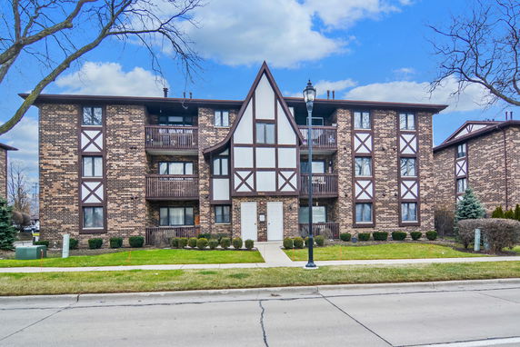 Front view of a multi-story brick apartment building with balconies and decorative wooden trim.