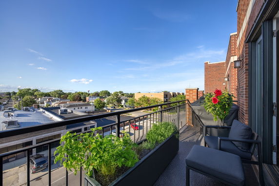 Panoramic view from a rooftop balcony with outdoor seating and planters, overlooking surrounding buildings and landscape.