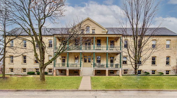 Front view of a multi-story building with a long porch and multiple windows.