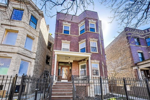 Front view of a multi-story brick building with a porch and iron fence.