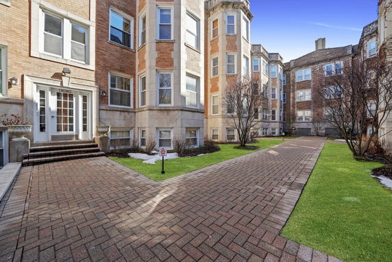 Front view of a multi-story brick apartment building with large windows and a central pathway.