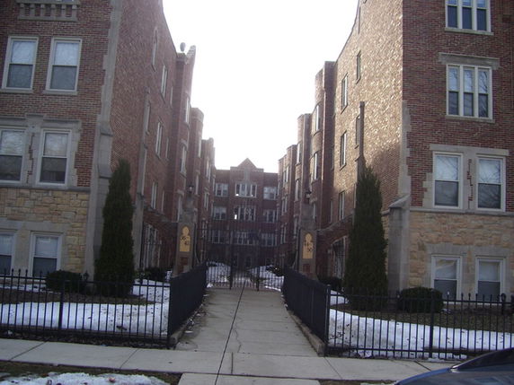 Front view of a multi-story brick apartment building with a gated entrance.