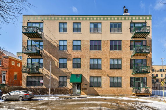 Front view of a multi-story brick apartment building with green window frames and balconies.