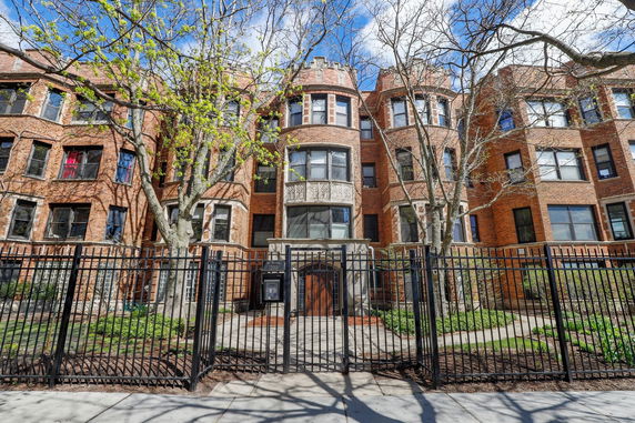 Front view of a multi-story brick building with distinctive bay windows and black iron fencing.