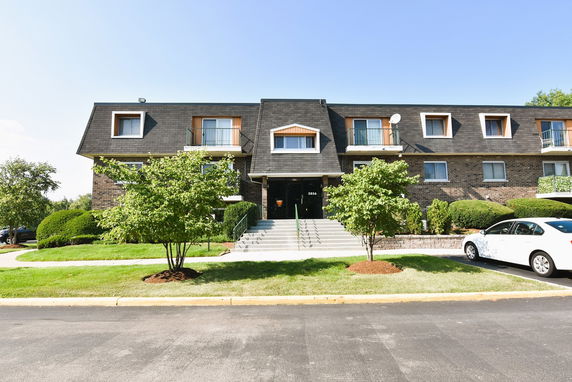 Front view of a multi-story apartment building with dark roofing and multiple windows.