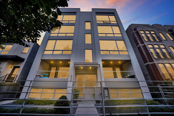 Front view of a modern multi-story building with large windows and a gated entrance.