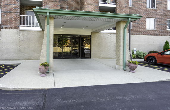 Entrance view of a building with a covered entryway, glass doors, and brick facade.