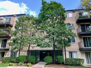 Front view of a multi-story apartment building with balconies and trees in front.