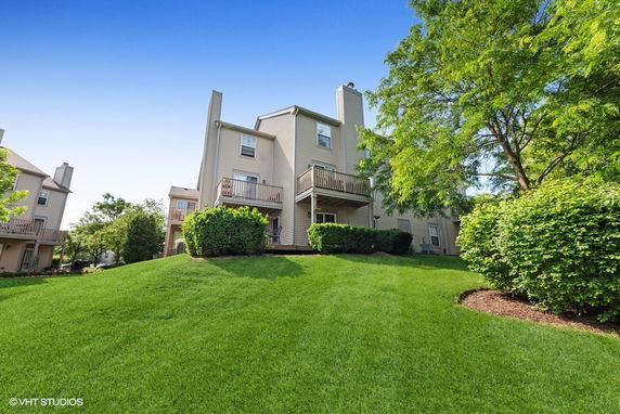 View of a multi-story house with balconies, surrounded by a lush lawn and trees.