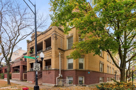 Front view of a brick multi-story residential building on a tree-lined street.