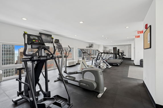 Indoor gym area with exercise equipment and windows overlooking the city.