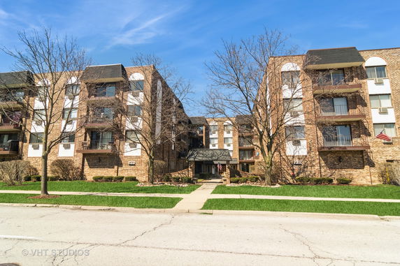 Front elevation view of a multi-story brick apartment building with balconies.