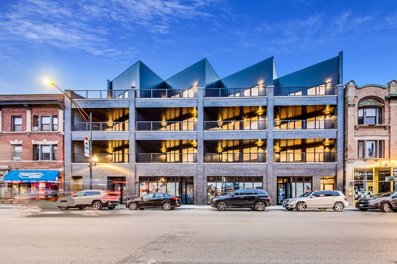 Front view of a modern multi-story building with large windows and a distinctive roof design.