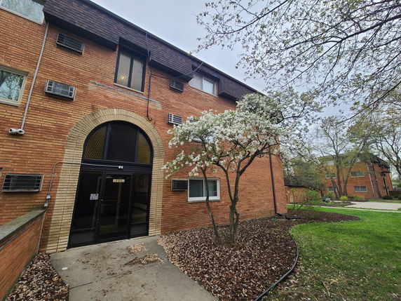 Front view of a brick apartment building with arched entryway and air conditioning units.