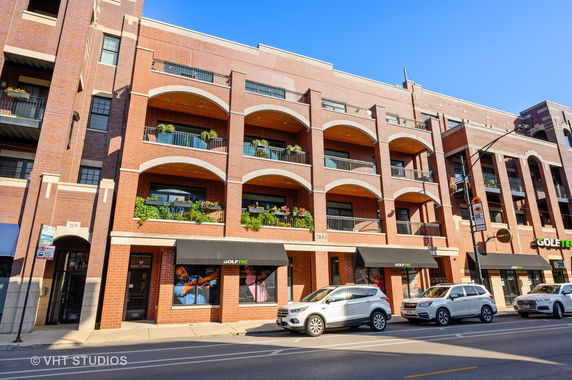 Front view of a multi-story brick building with balconies and storefronts.