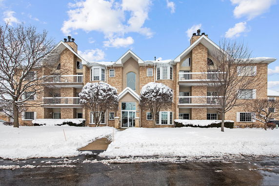 Front view of a multi-story brick apartment building with balconies and a central entrance, surrounded by snow.