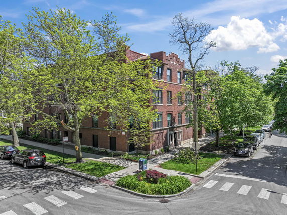 Front view of a multi-story brick building at a street corner with landscaped surroundings.