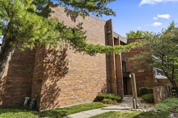 Front view of a brick building with a walkway and surrounding greenery.
