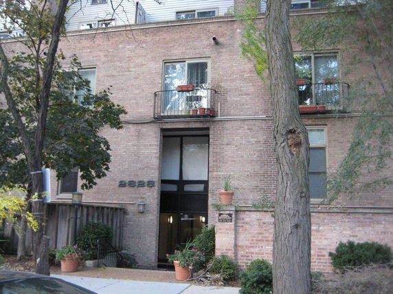 Front view of a multi-story brick building with balconies and potted plants.