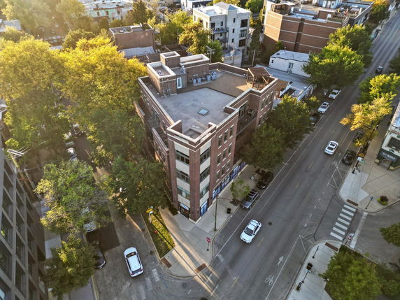 Aerial view of a multi-story building with a flat rooftop featuring air conditioning units and other structures.