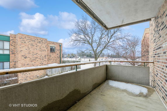 Balcony view overlooking neighboring brick buildings and a tree.