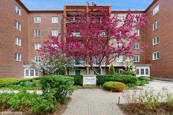 Front view of a multi-story brick condominium building with blooming trees.