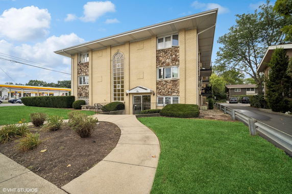 Front view of a multi-story apartment building with a distinct central arch window and mixed brick and stone facade.