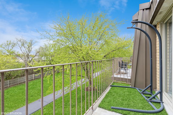 Balcony view overlooking a lush green garden with pathway and surrounding trees.