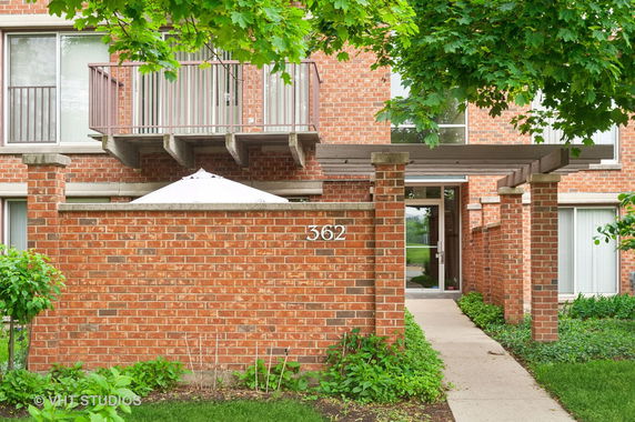 Front view of a brick building with a balcony and entrance with a pergola.