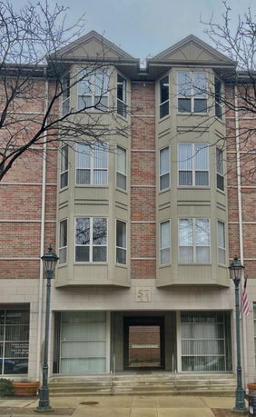 Front view of a multi-story brick building with large bay windows.