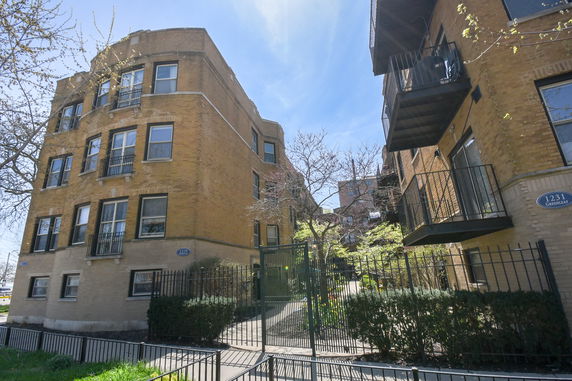 Front view of a multi-story brick building with balconies and a gated entrance.