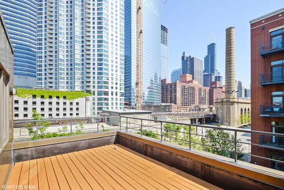 Rooftop with wooden deck, surrounded by tall buildings in an urban area.