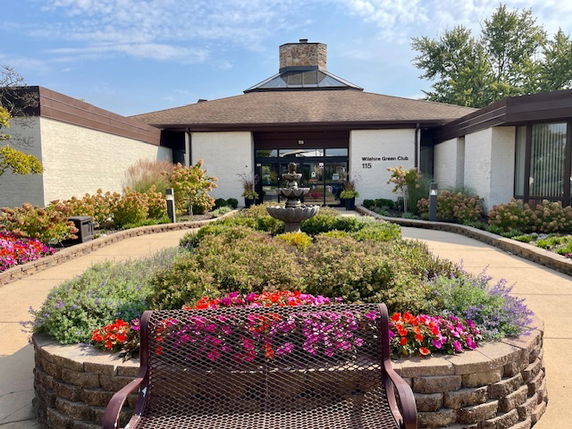 Front view of a single-story building with a triangular roof, garden, and bench.