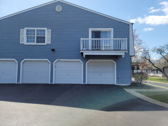 Front view of a blue house with three garage doors and a balcony.