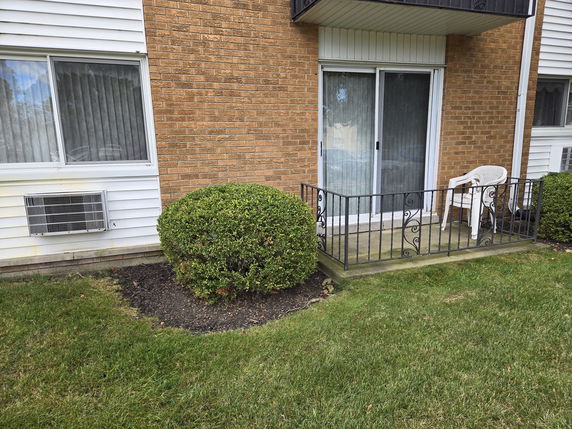 Exterior view of a building with a small balcony, sliding glass door, and adjacent window with an air conditioning unit.