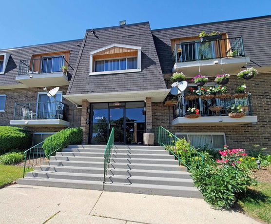 Front view of a multi-story residential building with balconies and decorative plants.