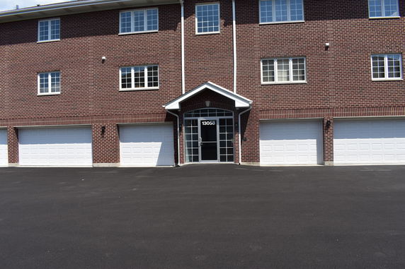 Front view of a brick multi-story building with multiple white garage doors and a central entrance.